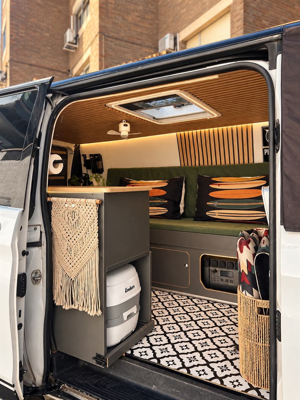 Interior de una furgoneta camper con techo de lamas de madera, sofá verde, cocina a medida y suelo de azulejo hidráulico