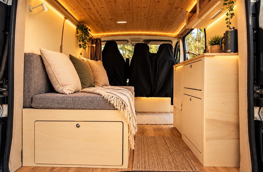 Interior de camper en madera de abedul con iluminación LED cálida, banco con almacenaje y cocina