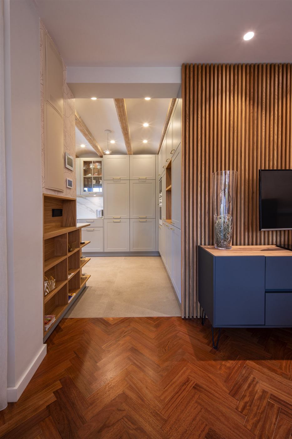 Vivienda reformada con pared de lamas de roble, mueble azul con tapa de madera, estanterías a medida, cocina lacada y suelo de parqué en espiga